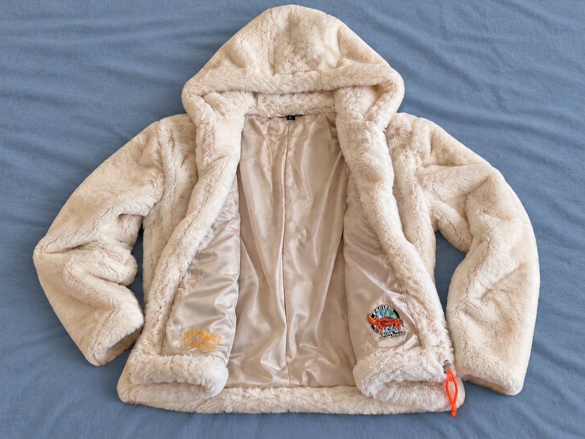 Open ivory hooded jacket on a faded blue bedspread showing satin interior, Pacific Claw logo and Second Wave marking